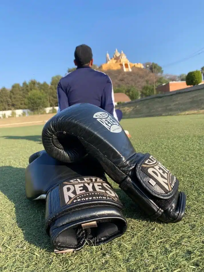Guantes de box sobre césped con vista a la iglesia de los Remedios en Cholula, representando entrenamiento al aire libre.