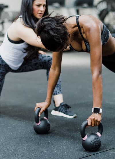 Entrenadora guiando a alumna en ejercicios de fuerza con kettlebells en gym de Cholula.